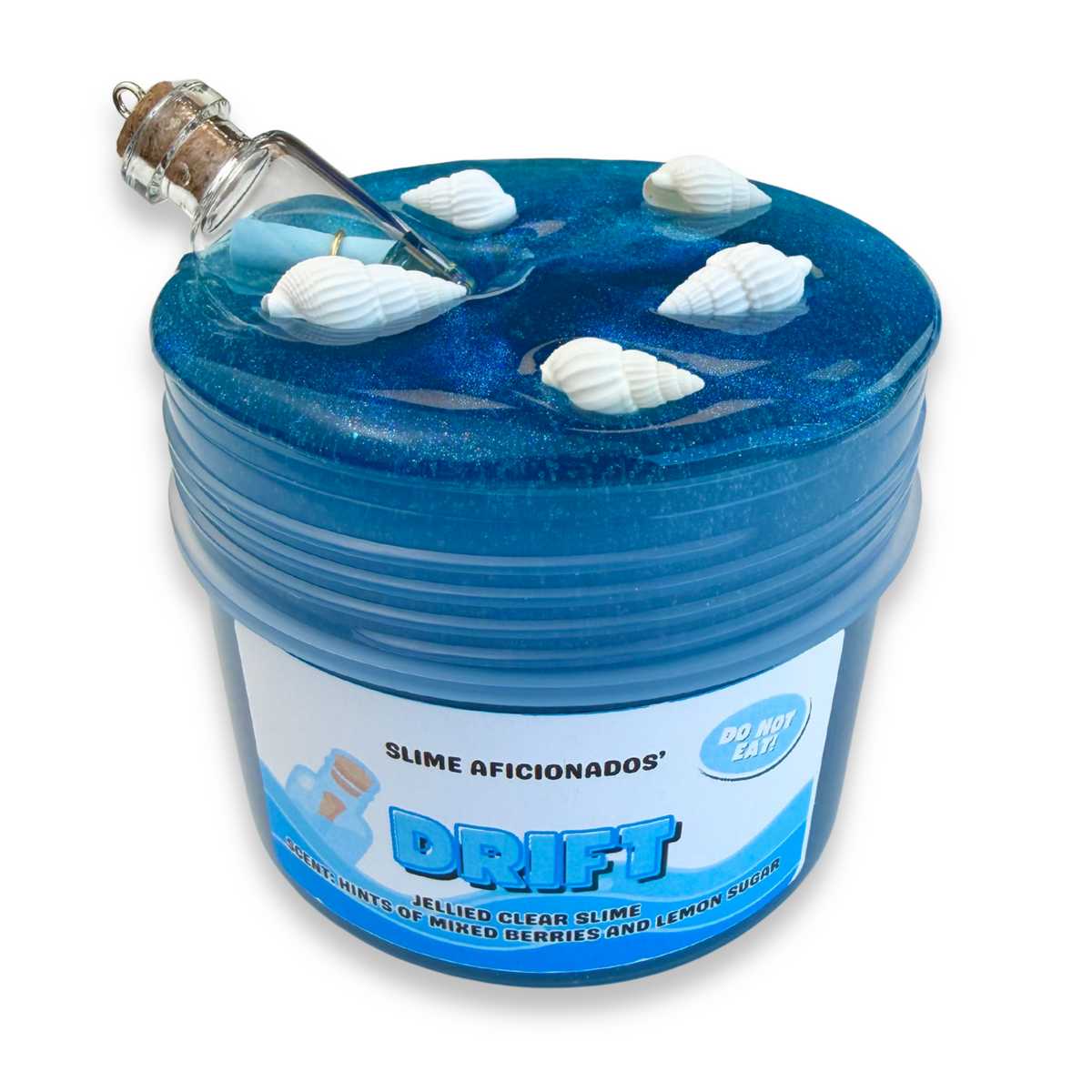 Ein schimmernder blauer Clear Slime mit einem Resin-Charm in Form eines Behälters mit einer Kork-Glasflasche am Deckel, zusammen mit weißen Muscheln obenauf, und einem Etikett vorne mit der Aufschrift „DRIFT“ und „SLIME AFICIONADOS“.