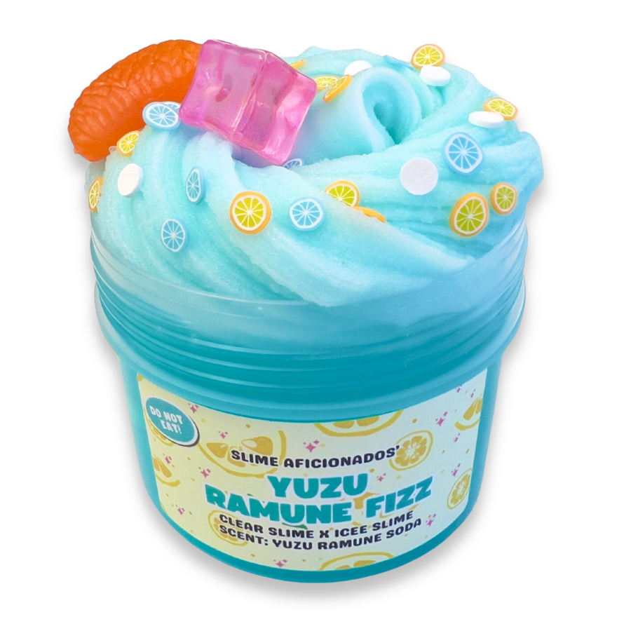 A jar of Yuzu Ramune Fizz slime, featuring light blue and turquoise swirled slime topped with a pink ice cube, a realistic 3D orange segment charm, and lemon clay slice decorations.