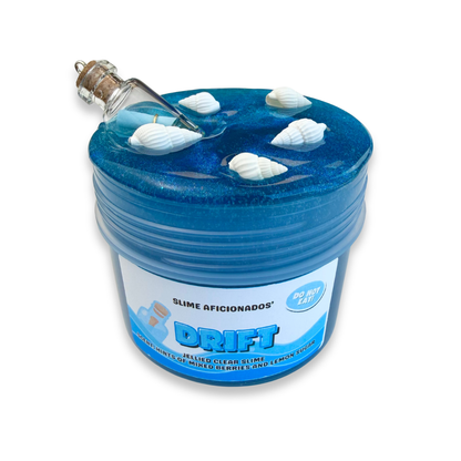 A shimmery blue clear slime, resin charm designed as a container with a cork-and-glass bottle attached to the lid, floating together with white seashells on top, and a front label reading 'DRIFT' and 'SLIME AFICIONADOS'.