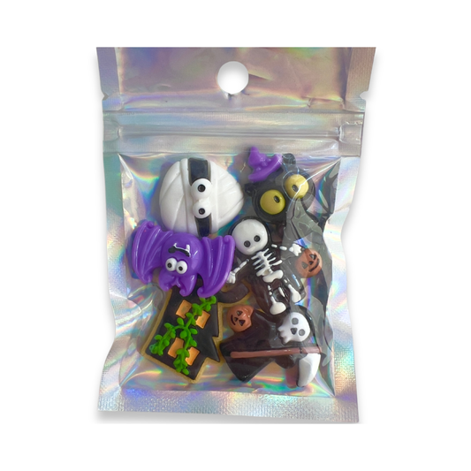 A small holographic zip-top pouch containing several Halloween-themed decorative charms or stickers, including a mummy, skeleton, witch, vampire, and pumpkin motifs, shown on a plain white background.