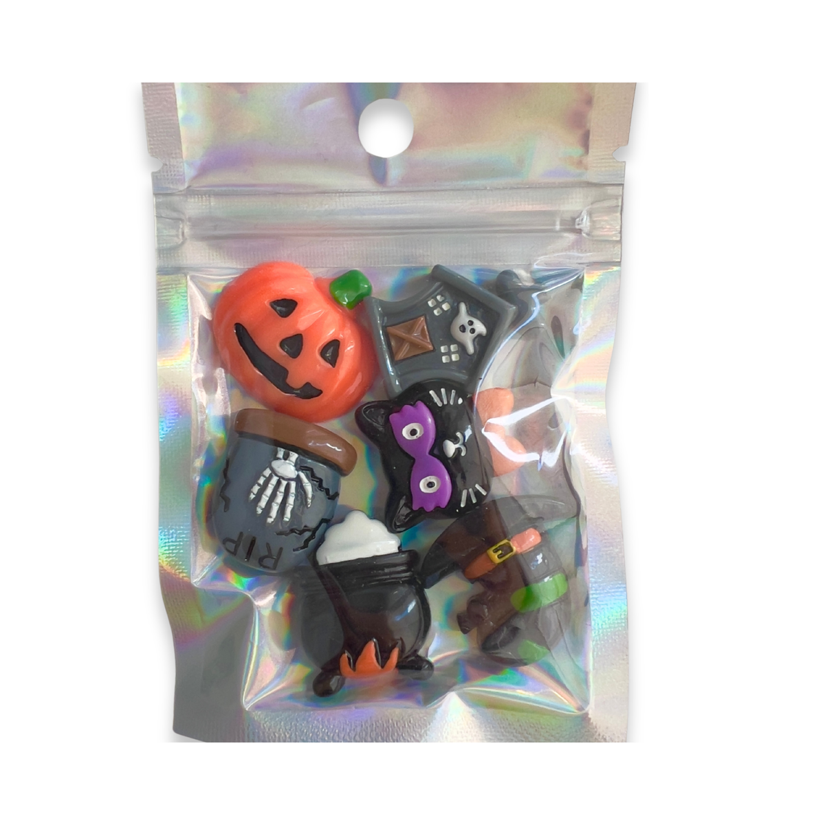 A set of five Halloween-themed cabochon charms in a clear, iridescent holographic zip-top bag. The charms include an orange jack-o'-lantern, a black cat with purple eyes, a gray cauldron with a skeleton, a black witch hat, and a black cauldron with orange flames.